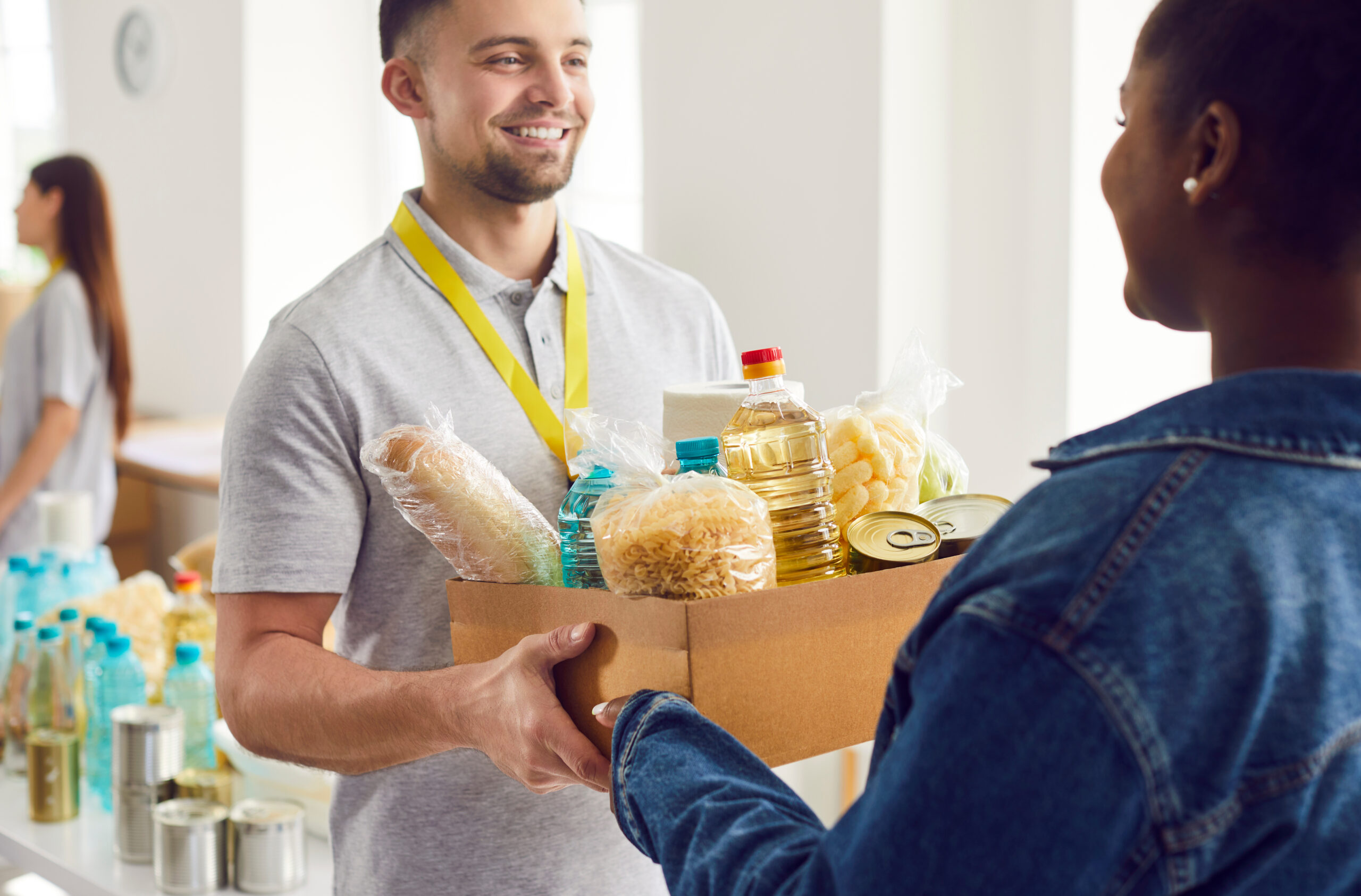 Un bénévole souriant remet un colis alimentaire à une personne dans le besoin dans un centre de distribution solidaire.